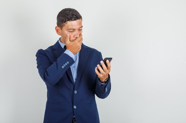 Joven mirando smartphone en traje y mirando sorprendido