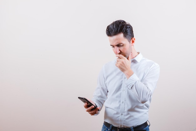 Joven mirando el teléfono móvil mientras piensa en camisa, jeans