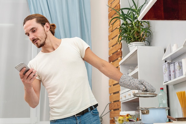 Foto gratuita joven mirando por teléfono y sosteniendo una olla de tapa