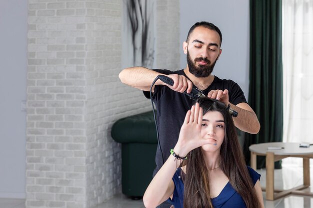 Una joven mirándose la mano mientras un peluquero le peina Foto de alta calidad