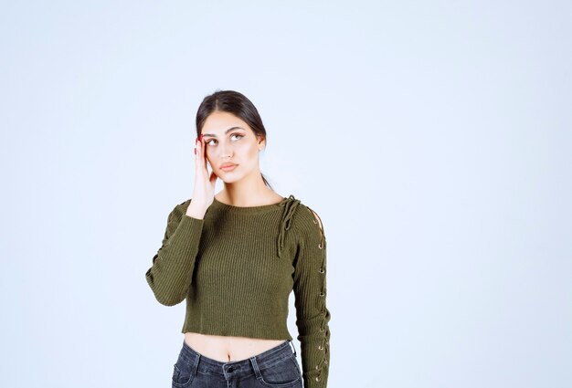 Una joven modelo en blusa verde pensando en algo sobre la pared blanca