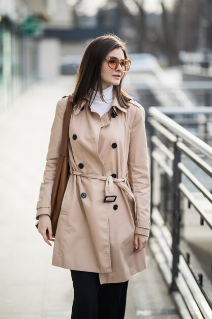 Joven modelo morena en gafas de sol transparentes caminar afuera en día de otoño