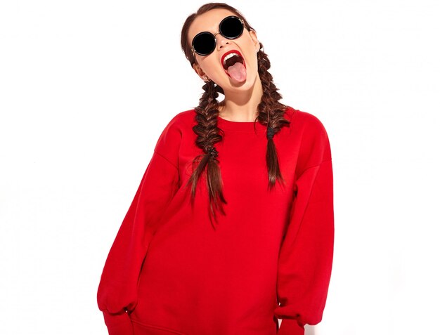 joven modelo de mujer sonriente feliz con maquillaje brillante y labios coloridos con dos coletas y gafas de sol en ropa de verano rojo aislado. mostrando su lengua