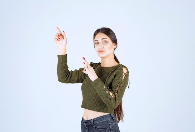 Joven modelo de mujer sonriente de pie y apuntando a un lado con los dedos índices