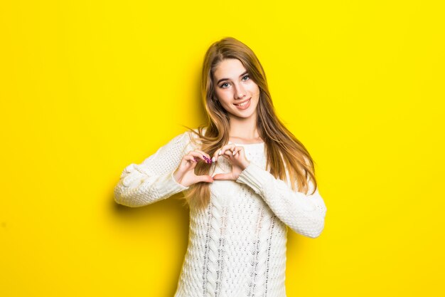 Joven modelo rubia en amarillo se enamora muestra el signo del corazón con las manos