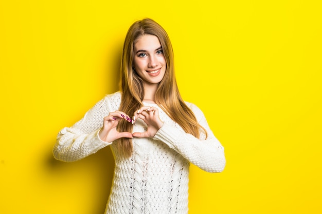 Joven modelo rubia en amarillo se enamora muestra el signo del corazón con las manos