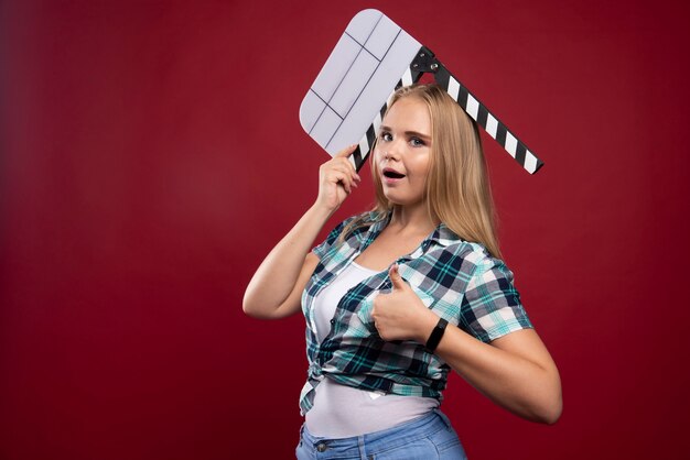 Joven modelo rubia sosteniendo una placa de chapaleta de filmación de películas en blanco y divirtiéndose.