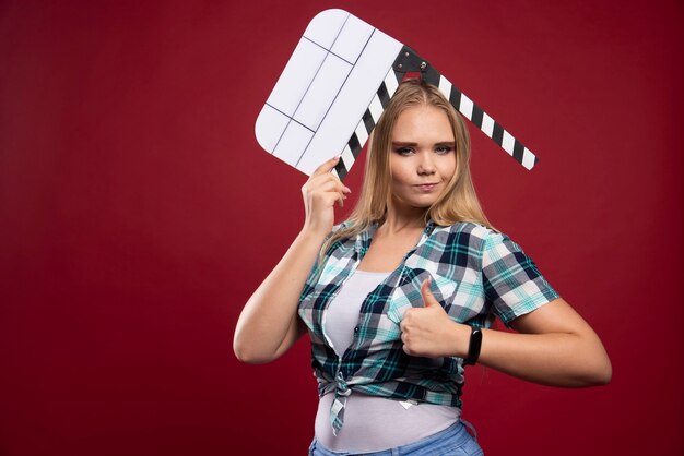 Joven modelo rubia sosteniendo una placa de chapaleta de filmación de películas en blanco y divirtiéndose.