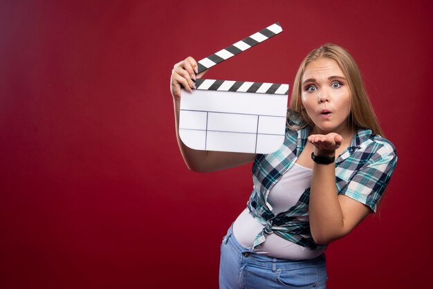 Joven modelo rubia sosteniendo una placa de chapaleta de filmación de películas en blanco y divirtiéndose.