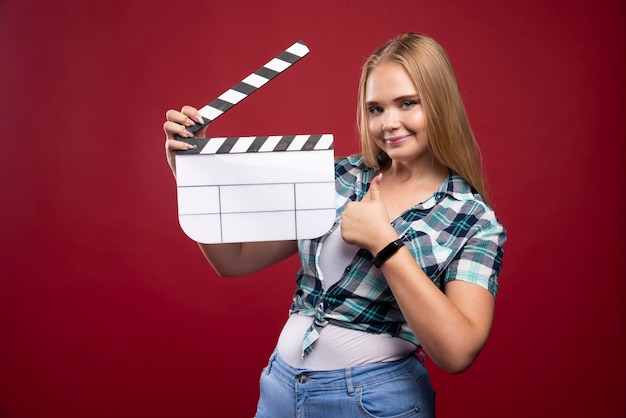 Joven modelo rubia sosteniendo una placa de chapaleta de filmación de películas en blanco y divirtiéndose.