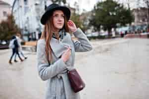 Foto gratuita joven modelo turista con abrigo gris y sombrero negro con bolso de cuero sobre los hombros en la calle de la ciudad