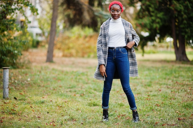 Joven, moderna, atractiva, alta y delgada, mujer musulmana africana con hiyab o turbante, bufanda y abrigo, posada en el parque