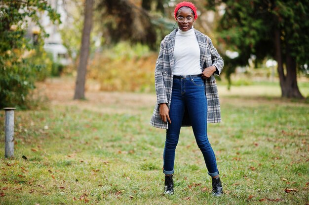 Joven, moderna, atractiva, alta y delgada, mujer musulmana africana con hiyab o turbante, bufanda y abrigo, posada en el parque