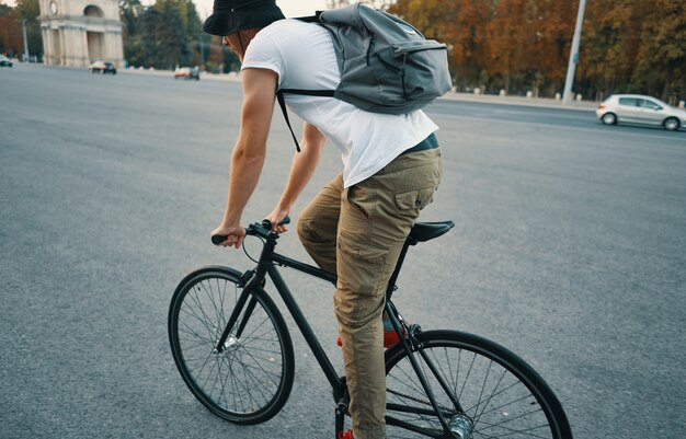 Joven moderno en bicicleta en una bicicleta clásica en la carretera de la ciudad con una mochila