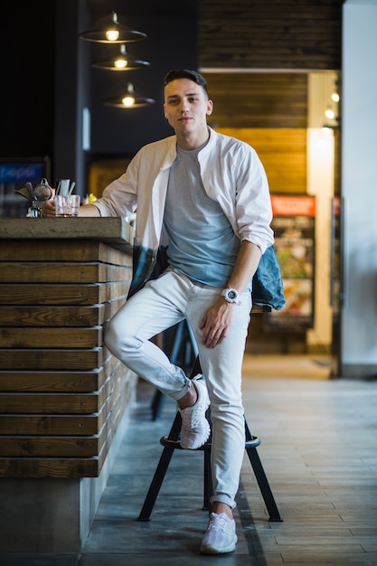 Joven moderno con vaso de whisky en la barra de bar