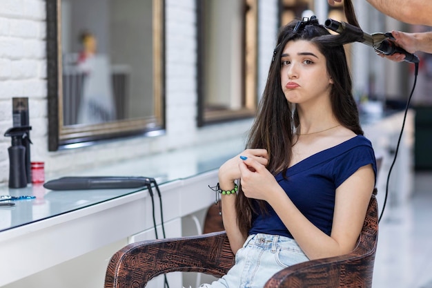 Una joven molesta sentada en la silla y mirando hacia otro lado mientras Barber se peina Foto de alta calidad