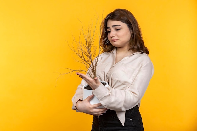 Una joven molesta sosteniendo una planta seca Foto de alta calidad