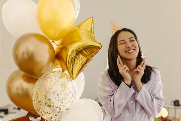 Joven morena asiática de piel clara con camisa cerrando los ojos cruza los dedos en su cumpleaños Concepto de emoción de la gente en la fiesta