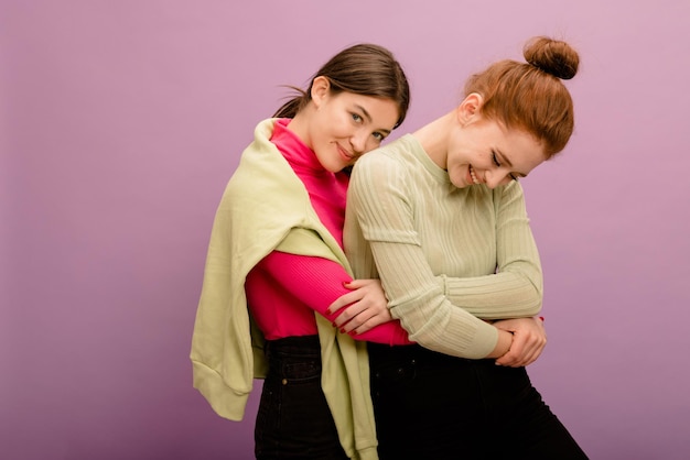 Foto gratuita una joven morena caucásica positiva con ropa informal abrazará a su novia pelirroja con un fondo morado personas emociones sinceras concepto de estilo de vida