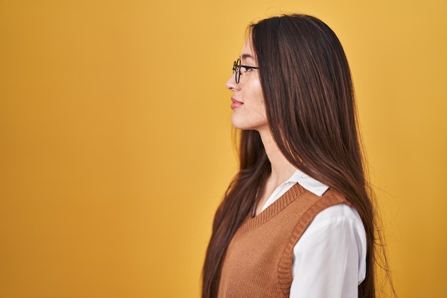 Foto gratuita joven morena de pie sobre un fondo amarillo con anteojos mirando hacia el lado relajado pose de perfil con cara natural con una sonrisa segura