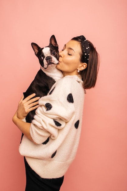 Joven morena de piel clara besa a su amado perro con fuerza mientras sostiene en brazos sobre fondo rosa Amor por las mascotas alegría y ternura