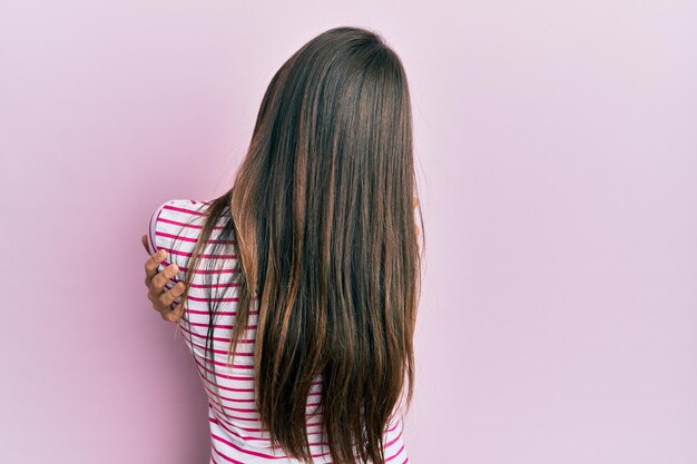 Joven morena con ropa informal de fondo rosa abrazándose feliz y positiva desde atrás. amor propio y cuidado propio