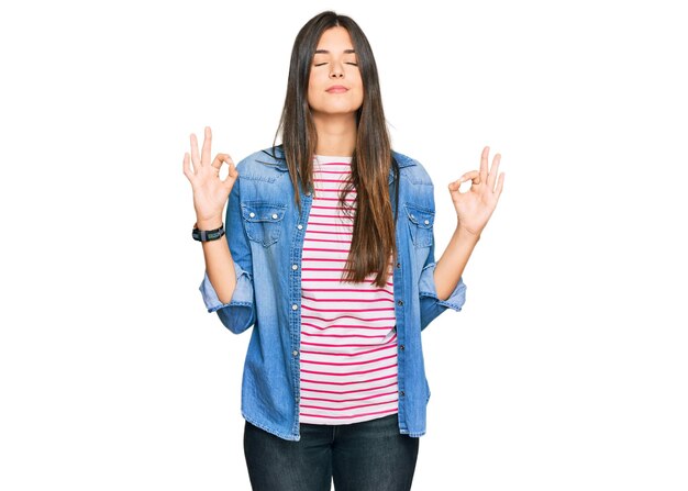 Joven morena con ropa informal relajada y sonriendo con los ojos cerrados haciendo gestos de meditación con los dedos. concepto de yoga