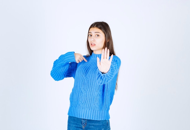 Foto gratuita joven morena en suéter azul dando señal de stop en blanco.