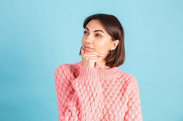 Joven morena en suéter rosa cálido aislado en la pared azul