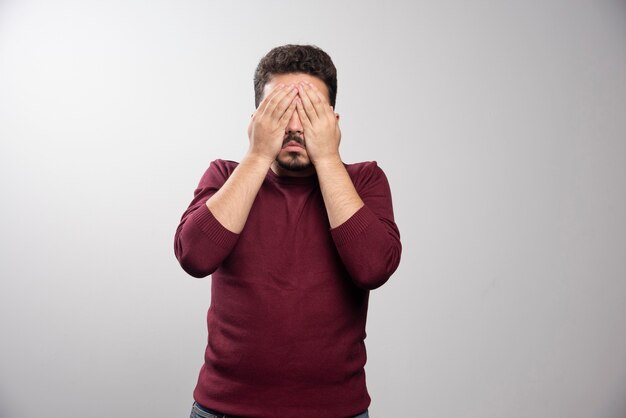 Un joven moreno tapándose los ojos y posando.