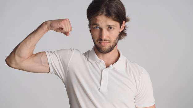 Joven mostrando bíceps mirando confiado sobre fondo blanco Chico deportivo demostrando fuerza corporal en la cámara