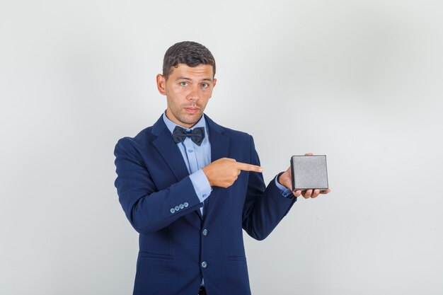 Joven mostrando caja de reloj con dedo en traje