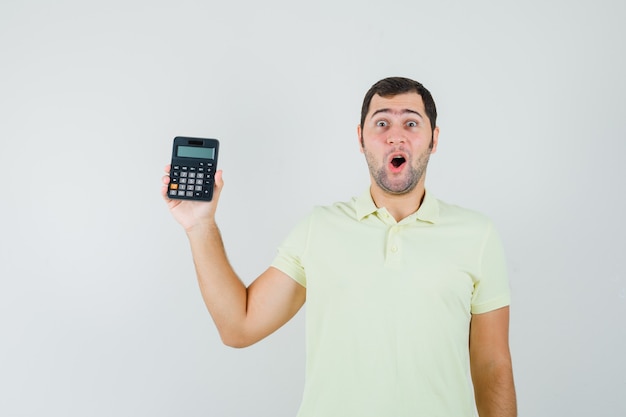 Joven mostrando calculadora en camiseta y mirando asombrado, vista frontal.