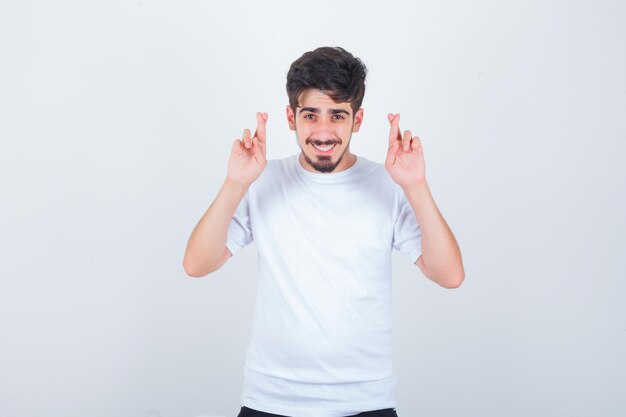 Joven mostrando los dedos cruzados en camiseta y luciendo lindo