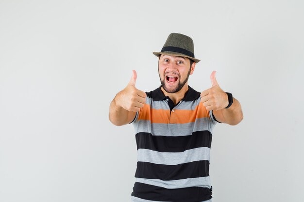 Joven mostrando doble pulgar hacia arriba en camiseta, sombrero y mirando feliz