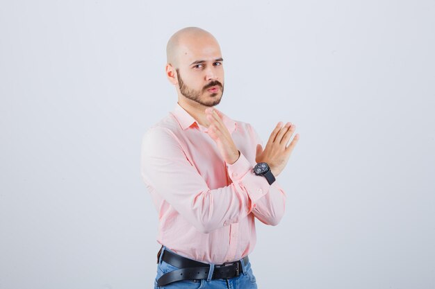 Joven mostrando gesto cerrado en camisa rosa, jeans y mirando serio.