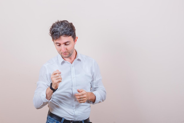 Joven mostrando gesto de dinero en camisa blanca, jeans y mirando enfocado