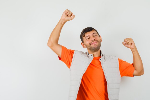 Joven mostrando gesto ganador en camiseta, chaqueta y mirando dichoso