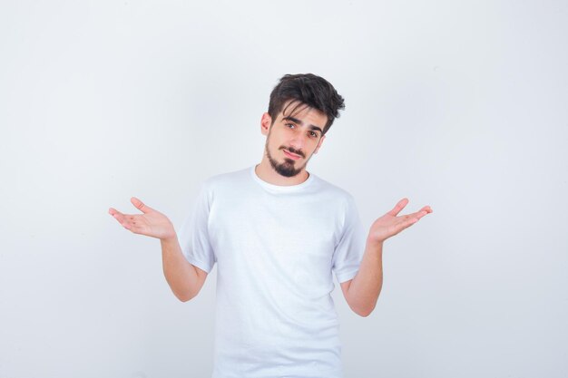 Joven mostrando gesto de impotencia en camiseta blanca y mirando confundido