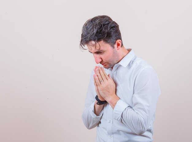 Joven mostrando gesto de namaste en camisa blanca y mirando esperanzado