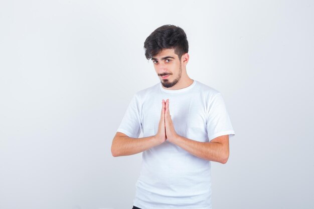 Joven mostrando gesto de namaste en camiseta y mirando esperanzado