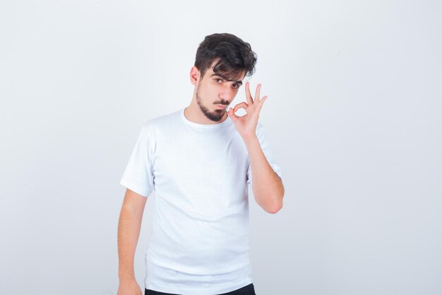 Joven mostrando gesto ok en camiseta y mirando confiado