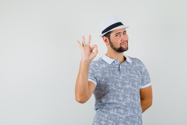 Joven mostrando gesto ok en camiseta, sombrero y mirando confiado. vista frontal.