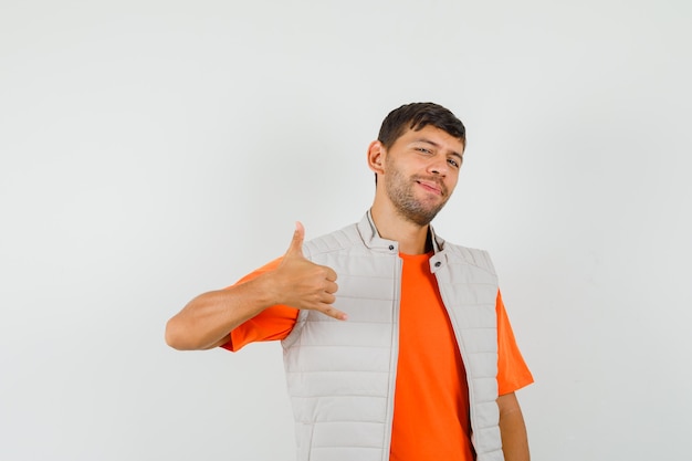 Joven mostrando gesto de teléfono en camiseta, chaqueta y mirando confiado.