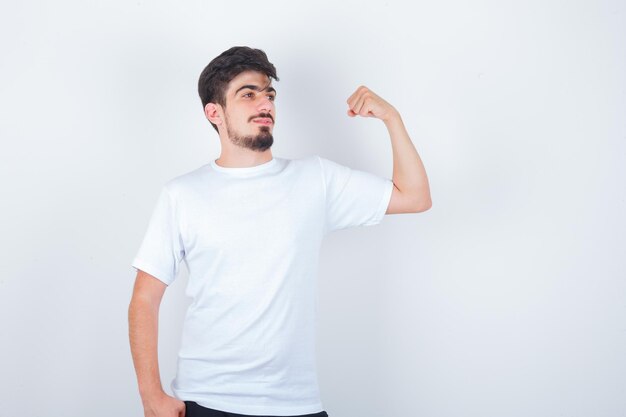 Joven mostrando los músculos del brazo en camiseta blanca y mirando confiado