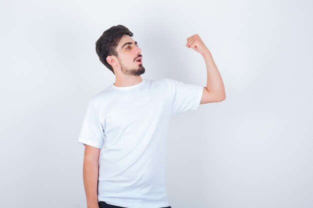 Joven mostrando los músculos del brazo en camiseta blanca y mirando confiado