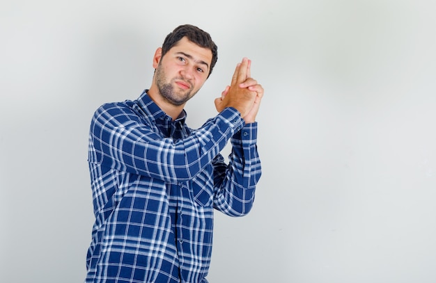 Foto gratuita joven mostrando pistola con las manos en camisa a cuadros y mirando confiado