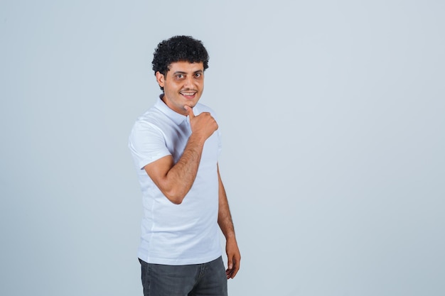 Joven mostrando el pulgar hacia arriba en camiseta blanca y jeans y mirando feliz, vista frontal.