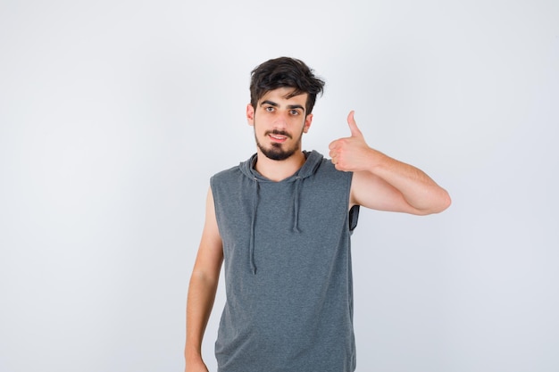 Joven mostrando el pulgar hacia arriba en camiseta gris y mirando serio