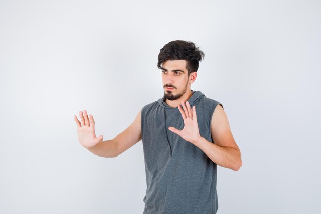 Joven mostrando señales de alto en camiseta gris y mirando serio